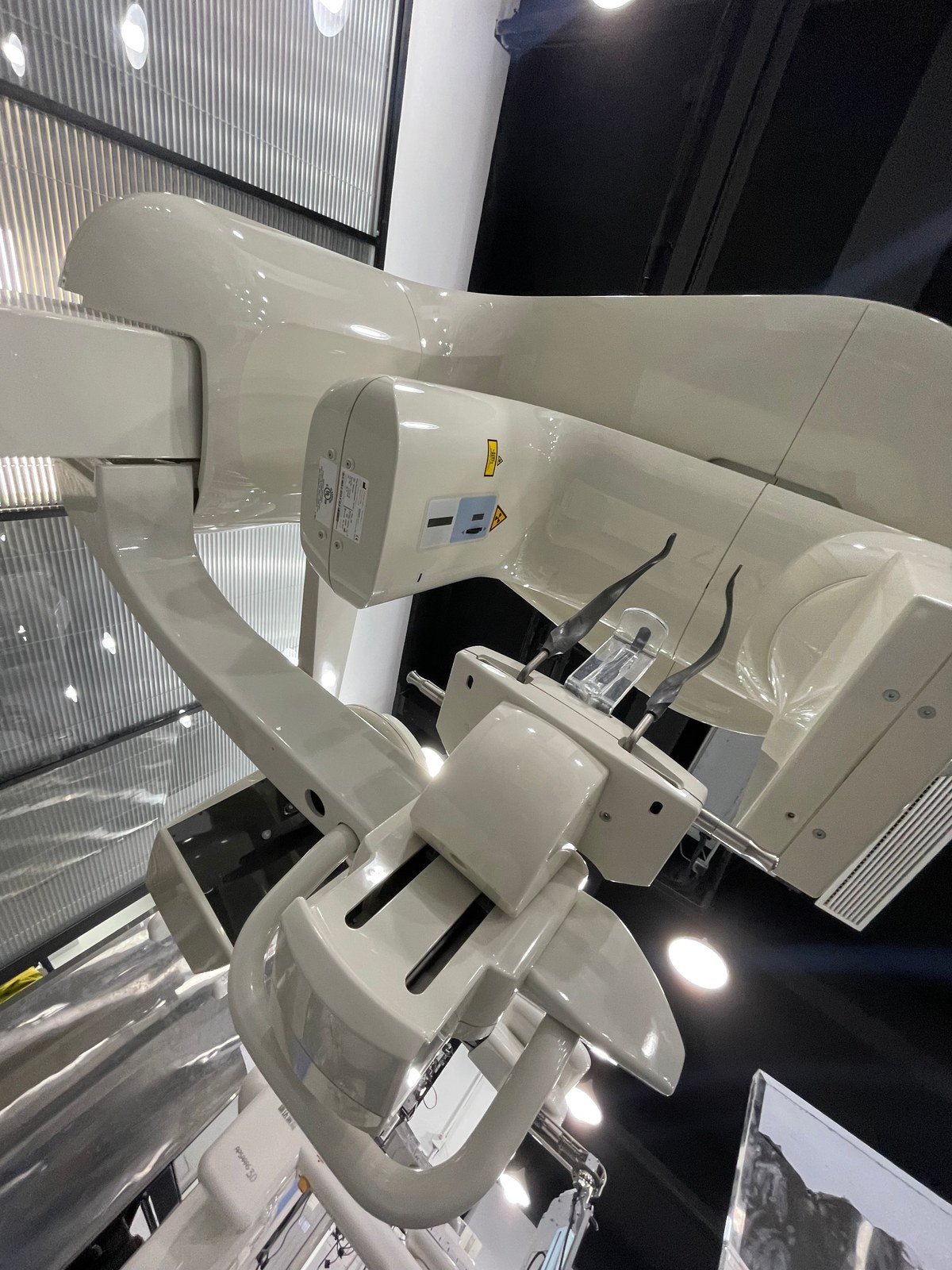 Carestream CS 9300 Select close-up of the rotating C-arm showing the X-ray tube housing with X-ray hazard label, the flat-panel detector assembly, patient positioner with carbon-fibre bite block stand and temple-stabilizer arms
