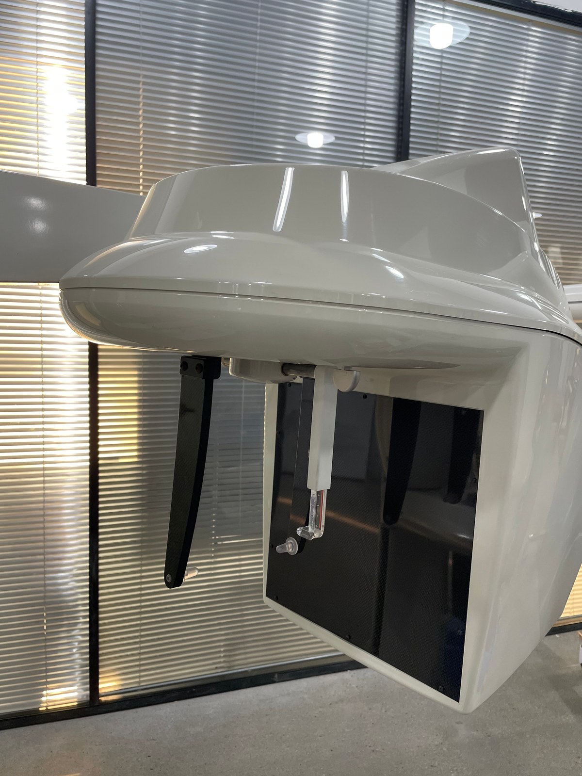 Close-up of the Carestream CS 9300 Select TFT flat-panel detector module showing the carbon-fibre imaging window, bite block support pillar, and the paired black carbon-fibre temple-stabilizer arms that keep the patient's head immobilized during acquisition