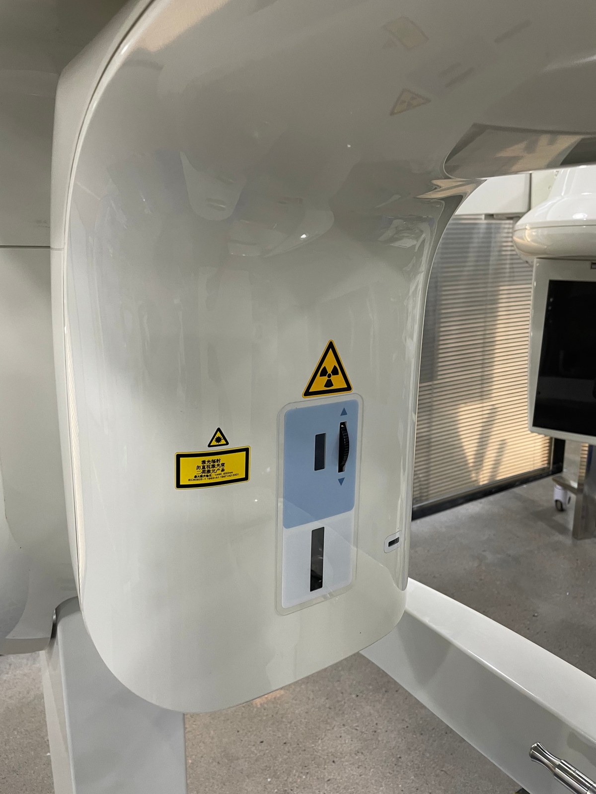 Detail of the Carestream CS 9300 Select side control panel — showing the yellow X-ray hazard warning label, laser safety compliance label (IEC 60825 class 2, 650 nm), and the tactile up/down movement controls for patient positioner height adjustment